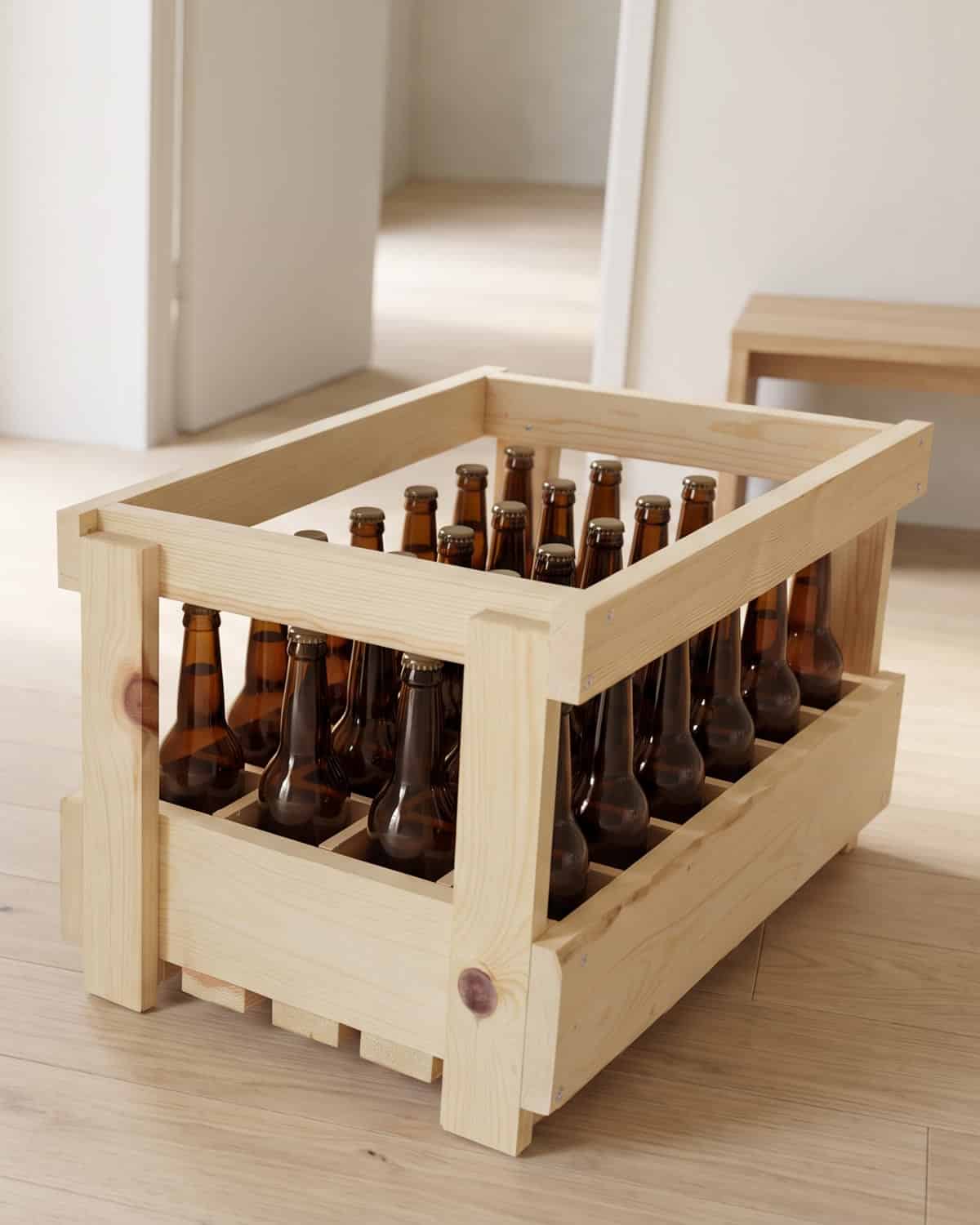 Casier à bière en bois pour 24 bouteilles long neck de 33 cl, rempli, posé sur le parquet clair d'une entrée