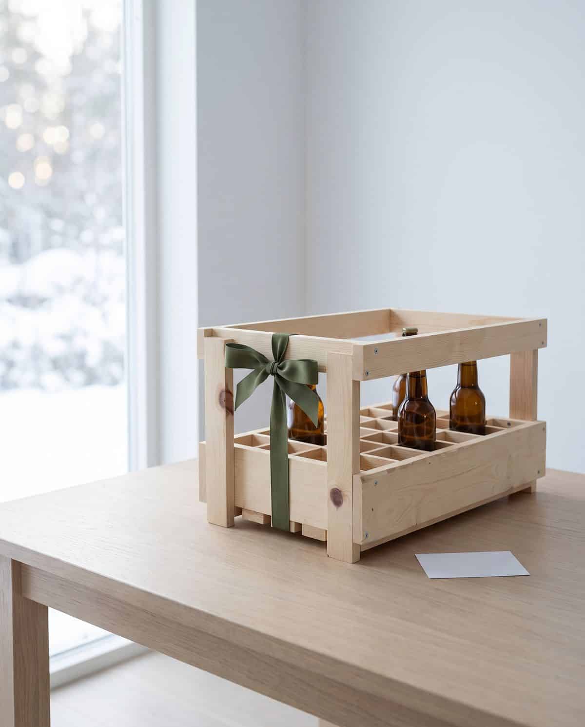 Casier à bière en bois de 24 cases noué d'un ruban vert, posé sur une table avec une carte, idée cadeau